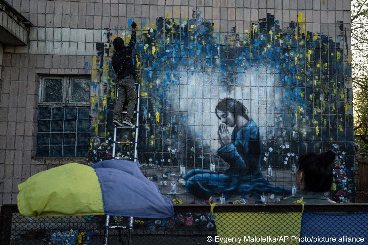 Bandit paints war mural in Bucha; widow beside it
