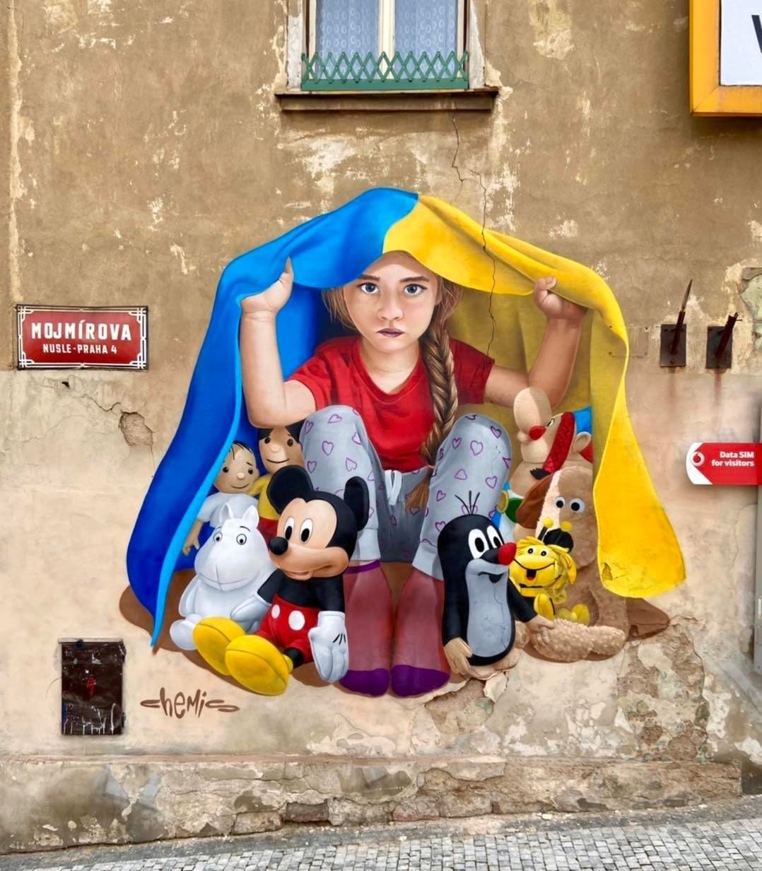 Prague mural: Sad girl protects toys under Ukrainian flag, symbolising war’s impact.
